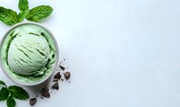 Mint chocolate chip ice cream scoop in white bowl garnished with fresh mint leaves and chocolate pieces on light background. Space for text.