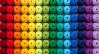 Colorful rainbow gradient of yarn balls arranged in organized rows from red to purple creating vibrant spectrum pattern for crafting and textile projects.
