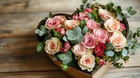Fresh pink and peach roses with eucalyptus leaves arranged in heart-shaped box on rustic wooden background, romantic floral composition for special occasions.
