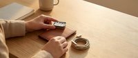 Person crafting leather goods at wooden workspace with tools and coffee cup in warm natural lighting for handmade artisan business concept.