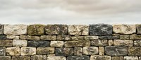Ancient stone wall with weathered limestone blocks in natural earth tones against cloudy sky background for construction and architectural projects.