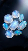 Collection of luminous opal gemstones displaying iridescent blue and green fire patterns on dark surface with dramatic lighting for jewelry design.
