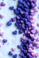 Small heart-shaped sugar candies in gradient colors from deep blue to soft pink scattered on white background, creating romantic Valentine's Day composition.