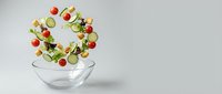 Fresh mixed salad ingredients flying into glass bowl with tomatoes, cucumbers, lettuce and herbs on white background for healthy eating concepts.
