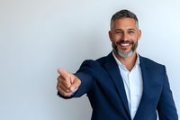 Confident mature businessman with gray beard wearing navy suit and white shirt showing thumbs up against light background, expressing positivity and success.