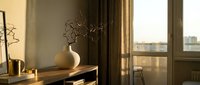 Modern minimalist interior with wooden console table, ceramic vase with dried branches, warm sunlight streaming through large windows creating shadows.