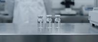Three clear glass vials arranged on laboratory counter in modern medical research facility for pharmaceutical development and scientific testing.