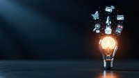 Glowing light bulb with digital technology icons floating above representing innovation, creativity and business ideas on dark background.