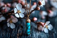 Turquoise crystal pendant necklace on gold chain against blooming cherry blossoms background, mystical jewelry photography on dark wooden surface.