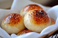Fresh baked dinner rolls with golden brown tops sprinkled with poppy and sesame seeds, served in white cloth napkin, close-up view showing soft texture.