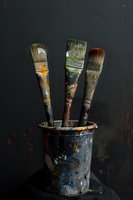 Used paintbrushes in black paint container against dark background, showing artistic texture and colorful paint residue on bristles and handles. Creative studio still life.