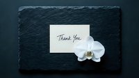 Elegant thank you card with white orchid flower on dark slate stone background, handwritten script, minimalist style for greeting and appreciation.