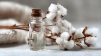 Small glass bottle with cork stopper next to natural cotton flowers on neutral background, creating rustic spa composition.
