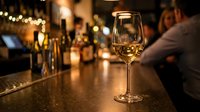 Elegant wine glass on bar counter in upscale restaurant with warm ambient lighting and blurred background creating sophisticated dining atmosphere.