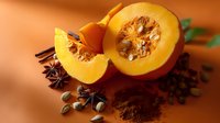 Fresh cut pumpkin with spices including star anise, cardamom pods and cocoa powder on warm orange background, macro food photography.