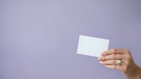 Female hand holding blank white business card against lavender background for branding, marketing, and corporate identity presentations.