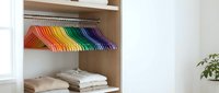 Organized wardrobe with colorful rainbow hangers and folded clothes on wooden shelves in modern minimalist closet interior for home organization.