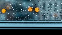 Raindrops on car window with blurred yellow street lights creating bokeh effect against dark moody background, dramatic weather atmosphere for seasonal concepts.
