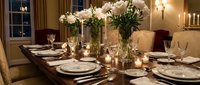 Elegant dining room table set for dinner party with white flowers, candles, fine china and crystal glasses creating luxurious atmosphere for entertaining.