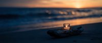 Glowing candle on driftwood at ocean beach during golden sunset with soft waves and warm sky colors creating peaceful romantic atmosphere for meditation.