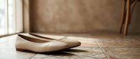 Elegant beige leather ballet flats on rustic wooden floor near window with natural lighting for fashion and footwear concepts.