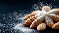 Raw almonds dusted with powdered sugar on dark background with bokeh effect, macro food photography for culinary and confectionery designs.