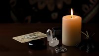 Mystical fortune telling setup with burning candle, tarot cards, crystal quartz and pentagram symbol on dark wooden table for spiritual guidance sessions.
