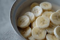 Fresh sliced bananas in white ceramic bowl, close-up view showing detailed texture and natural cross-section pattern of ripe fruit pieces for food styling.
