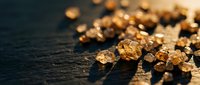 Golden amber crystals scattered on dark surface with shallow depth of field, suitable for luxury, jewelry, and premium product backgrounds.