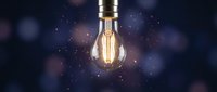 Vintage Edison bulb with warm glowing filament suspended against dark bokeh background with floating particles, symbolizing innovation, creativity, and bright ideas for design projects.