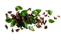 Fresh basil leaves scattered with dark chocolate pieces on white background, isolated food composition for culinary design and advertising.