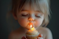 Caucasian toddler girl with blonde hair blowing out birthday candle on cupcake, closeup portrait with soft dreamy lighting and bokeh background.