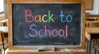 Colorful chalk text Back to School written on blackboard in classroom with wooden desks and chairs for education and learning concepts.