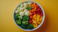 Fresh colorful vegetables arranged in white bowl including broccoli, cauliflower, carrots and bell peppers for healthy meal prep and cooking.
