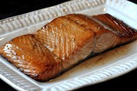 Glazed salmon fillet with caramelized surface on white plate, cooked seafood dish ready for gourmet dining and culinary presentation.