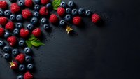Fresh mixed berries raspberries and blueberries scattered on dark slate background with mint leaves and copy space for healthy food design.