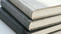 Stack of three linen-covered hardcover books in neutral gray tones on white surface, minimalist style for education, publishing, and design concepts.