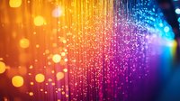 Vibrant glowing particles with colorful bokeh effect featuring orange, pink, purple and blue gradient background with magical sparkle trails and light streaks.