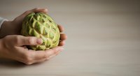 Fresh green custard apple held in hands on wooden surface, ready for healthy eating and nutrition content.