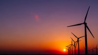 Wind turbines silhouetted against dramatic sunset sky with orange and purple hues. Renewable energy concept for sustainable power generation and clean technology.