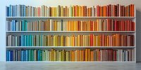 Books arranged by color spectrum on white modern shelves creating rainbow gradient effect from blue to red. Clean minimalist library interior design concept.
