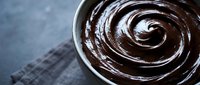 Rich dark chocolate ganache swirl in white bowl on textured slate surface for dessert recipes and culinary photography.