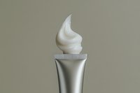 Creamy white cosmetic product swirled from silver tube against neutral beige background, showcasing luxury skincare texture for beauty advertising.