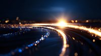Glowing light trails curve along dark background with blue and orange bokeh effects creating dynamic motion path at night, abstract technological concept.