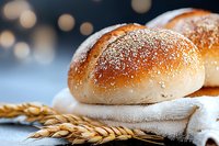 Fresh baked bread rolls dusted with flour on white linen cloth, with golden wheat ears in foreground and soft bokeh lights background, macro food photography.