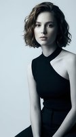 Young Caucasian woman with short wavy brown hair wearing elegant black asymmetrical dress against neutral background for fashion and lifestyle projects.