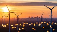 Wind turbines generating renewable energy at sunset with city skyline and bokeh lights creating sustainable power landscape for environmental projects.