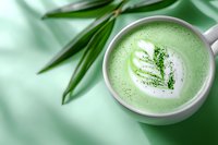 Green matcha latte with leaf art pattern in white ceramic cup on mint background with bamboo leaves, modern zen drink photography for cafe menu.
