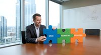Professional businessman assembling colorful puzzle pieces labeled sales, technology, operations in modern office conference room with city skyline view.