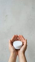Hands holding white cosmetic jar against neutral background, showcasing skincare product packaging for beauty, wellness, and dermatology applications.
